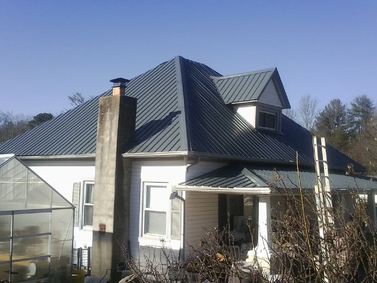 Dark blue standing seam metal roof on a white farmhouse with dormer — Slate & Tile Roof Repair by Roofing Brothers in Shelly