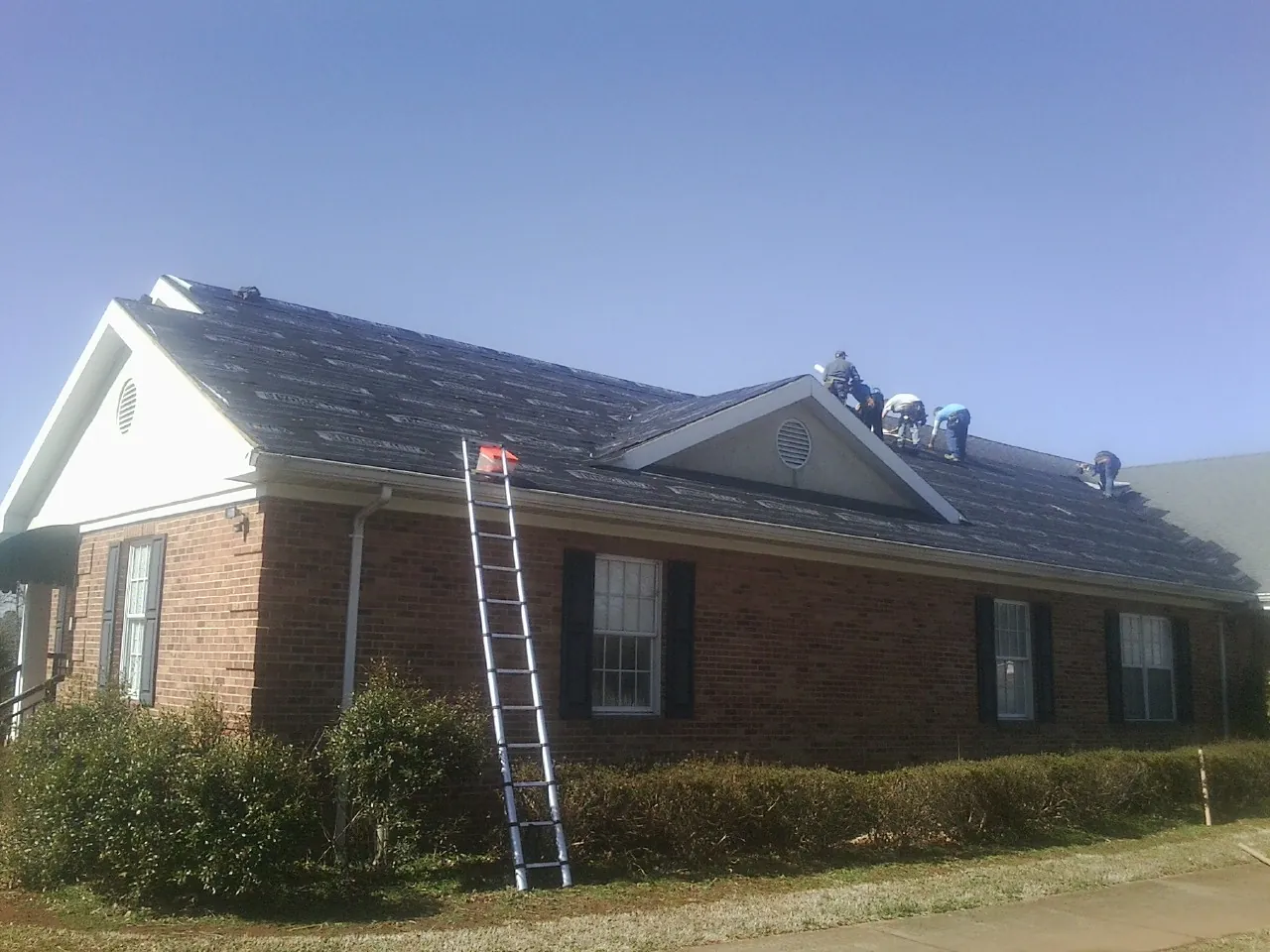 Crew tearing shingles off a brick ranch roof with a ladder set — Emergency Roof Repair work by our crew in Shelly