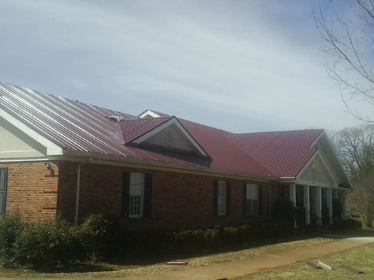 Red metal roof with gabled entries on a long brick building, from a Hail Damage Roof Repair job in Shelly