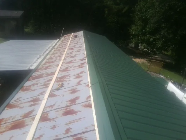Old rusted panels beside newly installed green metal roofing — Wind Damage Roof Repair by Roofing Brothers in Shelly
