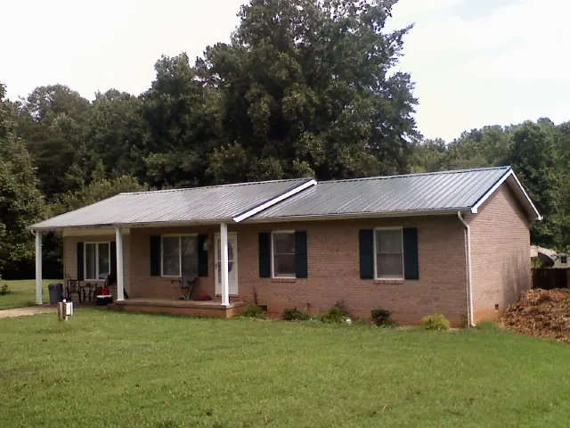 Gray metal roof on a brick ranch house with a side carport in Shelly