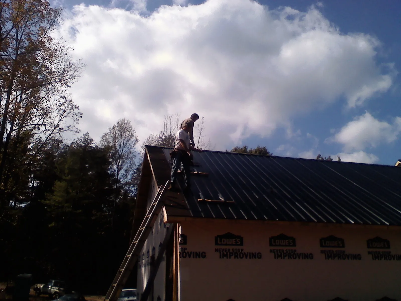 Roofer fastening dark metal panels high against a cloudy sky, from a Roof Inspection job in Shelly