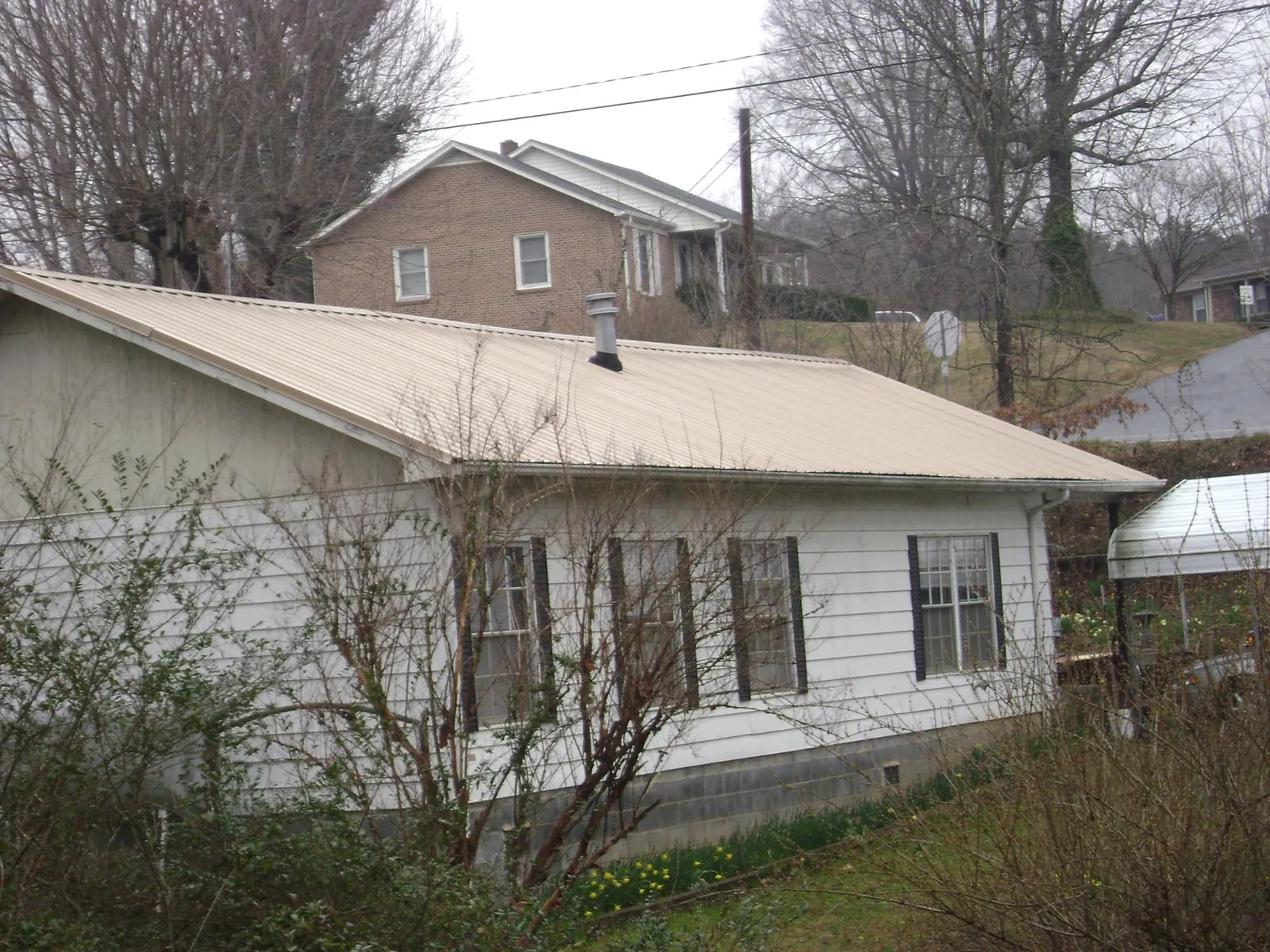 Tan metal roof on a white sided house set into a hillside — Commercial Roofing by Roofing Brothers in Shelly